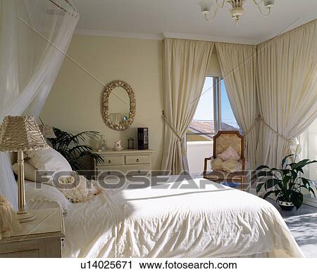 Stock Image - Cream bedlinen and curtains in Spanish bedroom. Fotosearch