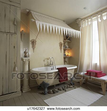 Stock Photo - Cream canopy above rolltop bath in cream bathroom with classical column. Fotosearch