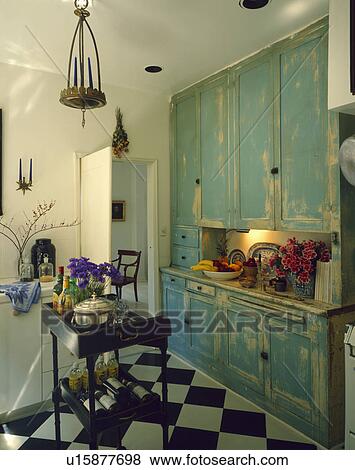Distressed paint-effect turquoise cupboard in white kitchen with chequerboard flooring View Large Photo Image Stock Photo - Distressed paint-effect turquoise cupboard in white kitchen with chequerboard flooring. Fotosearch