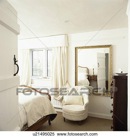 Stock Photography - Door open to cream tub chair and large mirror in cream country bedroom. Fotosearch