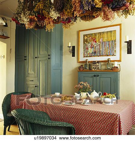 Picture - Dried flowers on ceiling above table with pink cloth in dining room with blue cupboard. Fotosearch