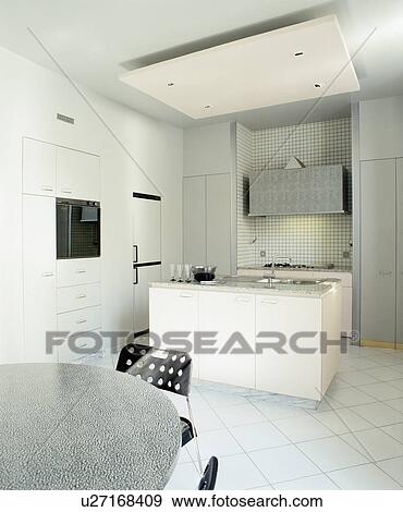 Stock Photo - False ceiling above island unit in modern white kitchen with granite-topped table and white tiled floor. Fotosearch