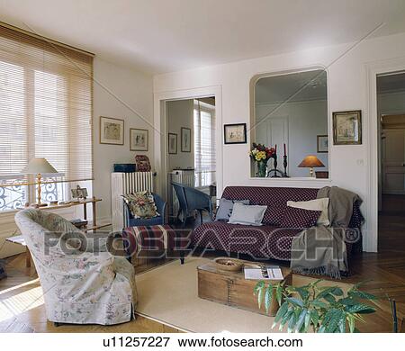 Stock Photo - Floral loosecover on armchair in French apartment living room with red quilt on sofa. Fotosearch