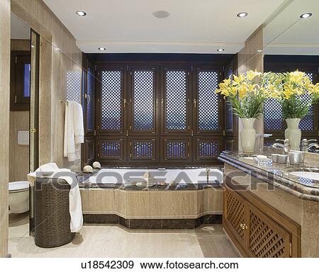 Stock Photo - Fretwork shutters on window above bath in modern marble bathroom. Fotosearch