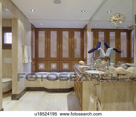 Stock Photography - Fretwork shutters on window above bath in modern marble bathroom. Fotosearch