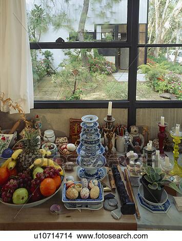 Picture - Fruit in bowl and collection of candles and china below window with view of garden. Fotosearch