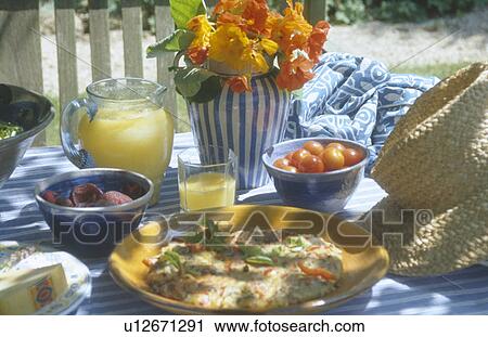 Stock Image - Fruit-juice in glass jug on garden table with omelette on plate and orange nasturtiums in vase. Fotosearch