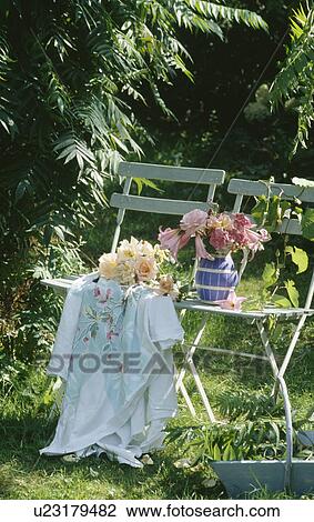 Stock Image - Garden chairs with old tablecloth and pink flowers in blue+white jug. Fotosearch