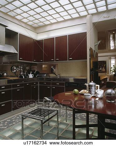 Glass brick ceiling and floor in modern kitchen with black units and traditional dining table with chrome teapot View Large Photo Image Picture - Glass brick ceiling and floor in modern kitchen with black units and traditional dining table with chrome teapot. Fotosearch