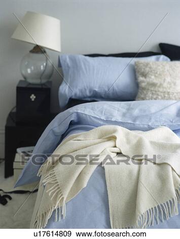 Glass lamp on bedside table beside bed with blue bedline and cream wool throw View Large Photo Image Stock Photo - Glass lamp on bedside table beside bed with blue bedline and cream wool throw. Fotosearch