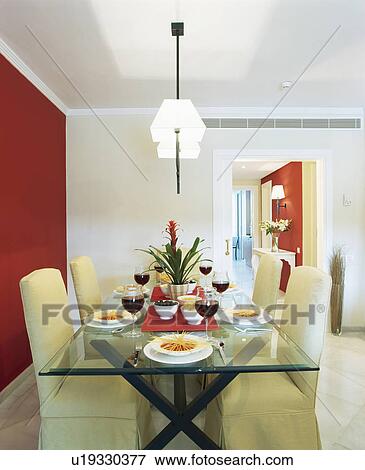 Glass-topped table and upholstered white chairs in white dining room with red wall View Large Photo Image Stock Photo - Glass-topped table and upholstered white chairs in white dining room with red wall. Fotosearch
