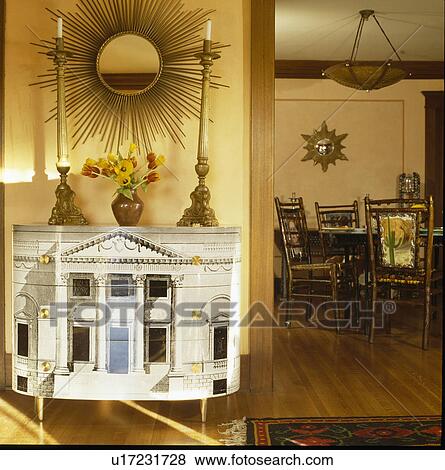 Gold sunburst mirror above Fornasetti cabinet in neutral dining room View Large Photo Image Stock Photo - Gold sunburst mirror above Fornasetti cabinet in neutral dining room. Fotosearch