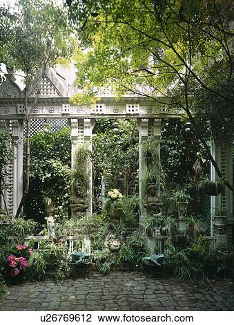 Stock Image - Green hanging plants and stone gazebo in lush green courtyard. Fotosearch