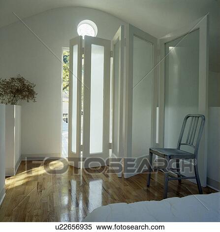 Grey metal chair in modern white bedroom with folding glazed doors and wooden floor View Large Photo Image Stock Photography - Grey metal chair in modern white bedroom with folding glazed doors and wooden floor. Fotosearch