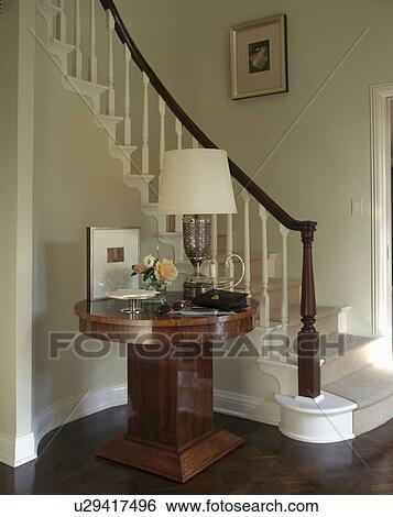 Lamp on circular antique table beside curved staircase in traditional hall View Large Photo Image Stock Photograph - Lamp on circular antique table beside curved staircase in traditional hall . Fotosearch