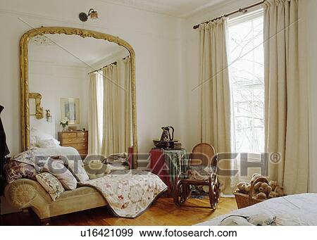 Large gilt antique mirror above chaiselongue in spacious bedroom with cream curtains View Large Photo Image Stock Photo - Large gilt antique mirror above chaiselongue in spacious bedroom with cream curtains. Fotosearch