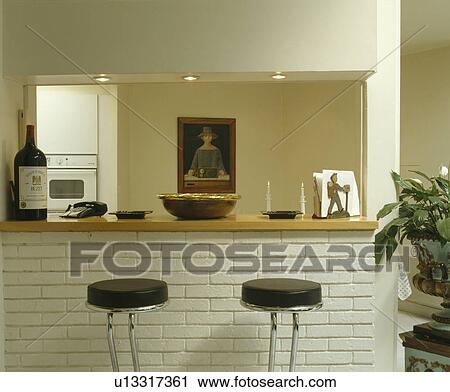 Stock Image - Leather and chrome stools at breakfast bar in modern white kitchen. Fotosearch