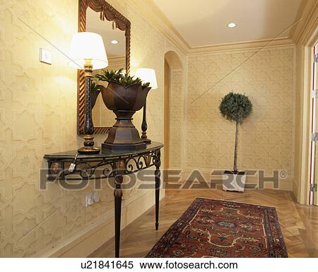 Stock Photography - Lighted lamps on metal console table in cream hall. Fotosearch