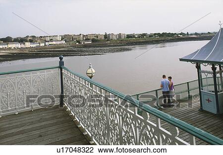 Stock Image - Looking down from ornate iron railings on young couple on the pier at Cleveland in Somerset. Fotosearch