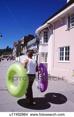 Picture - Man carrying green and purple inflatable rubber rings in street outside pink house at Lyme Regis in Dorset. Fotosearch
