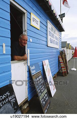 Picture - Man looking out of blue office hut for beach hut hire. Fotosearch
