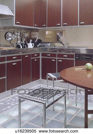 Metal stools and wood table on glass brick floor in modern kitchen with dark brown fitted units View Large Photo Image Stock Photography - Metal stools and wood table on glass brick floor in modern kitchen with dark brown fitted units. Fotosearch