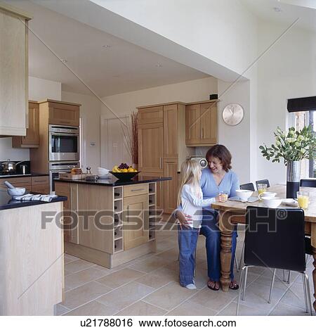 Stock Photograph - Mother and small girl at dining table in modern kitchen. Fotosearch