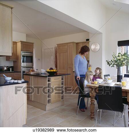 Stock Photo - Mother and two small girls at table in modern kitchen. Fotosearch
