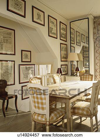 Stock Photo - Neutral-checked upholstered chairs and simple wood table in small dining room with tall mirror and collection of pictures. Fotosearch