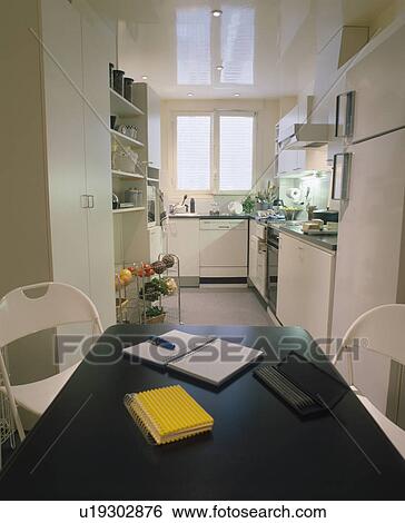 Stock Photograph - Notebooks and pen on black table with white chairs in modern white kitchen. Fotosearch