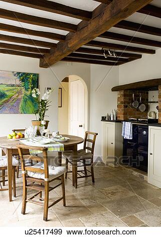 Stock Photo - Oak country chairs and table in cream kitchen with travertine flooring and beamed ceiling. Fotosearch