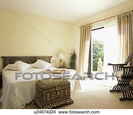 Ornate chest below bed with white bedlinen in cream bedroom View Large Photo Image Picture - Ornate chest below bed with white bedlinen in cream bedroom. Fotosearch