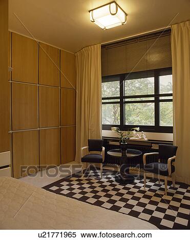 Panelled Wall And Thirties Light In Bedroom With Black White Chequerboard Rug And Brown Blind With Cream Curtains Stock Photography