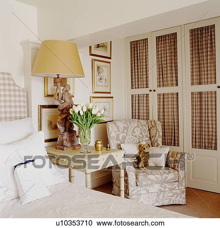 Stock Image - Patterned armchair in front of fitted wardrobe in cream bedroom. Fotosearch