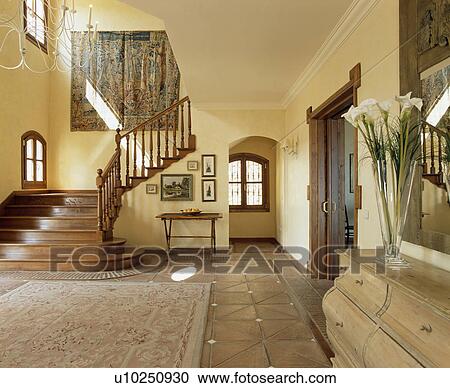 Stock Image - Patterned rug on terracotta floor tiles in large Spanish hall with tapestry on wall. Fotosearch