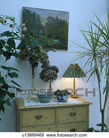 Stock Photo - Picture above chest-of-drawers with lighted lamp and dried flowers in vase. Fotosearch