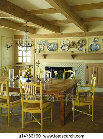 Stock Image - Rectangular antique wooden table with rush seated chairs in traditional neutral dining room with beamed ceiling. Fotosearch