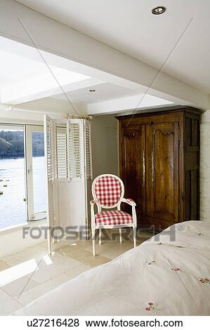 Red+white checked chair and large rdrobe in bedroom with white screen in front of window with view of the sea View Large Photo Image Stock Photo - Red+white checked chair and large rdrobe in bedroom with white screen in front of window with view of the sea. Fotosearch