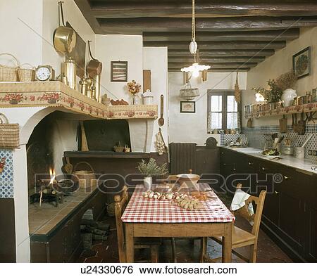 Stock Photograph - Red+white oilcloth on pine table in front of fireplace in old country kitchen. Fotosearch