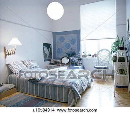 Picture - Retractable wall-light and paper lampshade above bed with blue checked and striped quilt and bedlinen in blue bedroom. Fotosearch