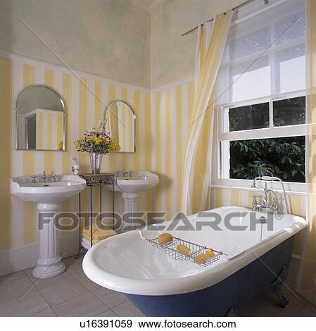 Roll-top bath in front of open window with white blind in bathroom with yellow striped wallpaper and double basins View Large Photo Image Stock Photo - Roll-top bath in front of open window with white blind in bathroom with yellow striped wallpaper and double basins. Fotosearch