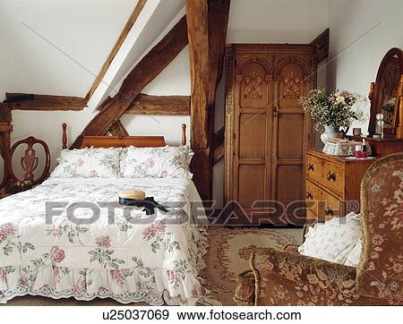 Stock Photo - Rose-patterned quilt and antique wardrobe in beamed country bedroom. Fotosearch