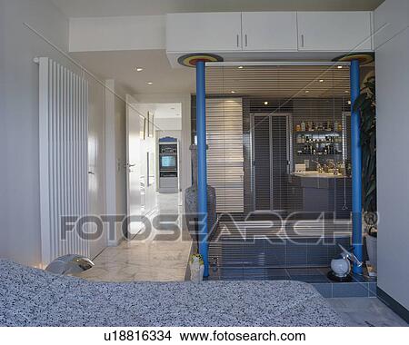 Slatted blinds dividing small blue ensuite bathroom from modern townhouse bedroom with vertical white radiator View Large Photo Image Picture - Slatted blinds dividing small blue ensuite bathroom from modern townhouse bedroom with vertical white radiator. Fotosearch