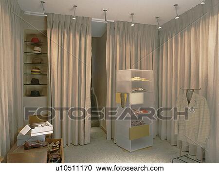 Stock Image - Spotlights above perspex shelving and beige curtains concealing storage. Fotosearch