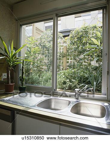 Stainless steel double sink in front of large window with view of small courtyard with green plants View Large Photo Image Stock Image - Stainless steel double sink in front of large window with view of small courtyard with green plants. Fotosearch