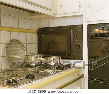 Stock Photo - Stainless steel saucepans on steel hob beside built-in microwave and oven. Fotosearch