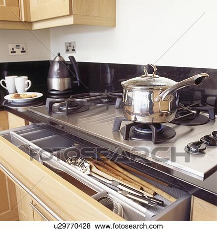 Stock Photo - Steel saucepan on stainless steel hob above open cutlery drawer. Fotosearch