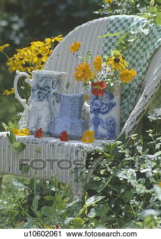 Stock Image - Still-life of blue+white china jugs on old white Lloyd Loom chair in garden. Fotosearch