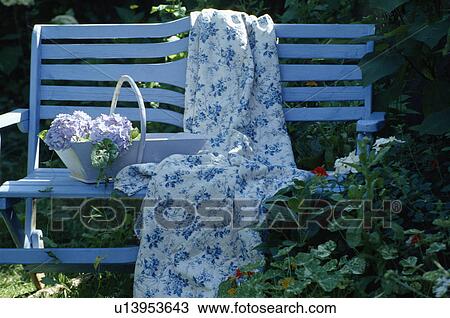 Stock Image - Still-life of blue+white quilt and pale blue trug on painted blue garden bench. Fotosearch