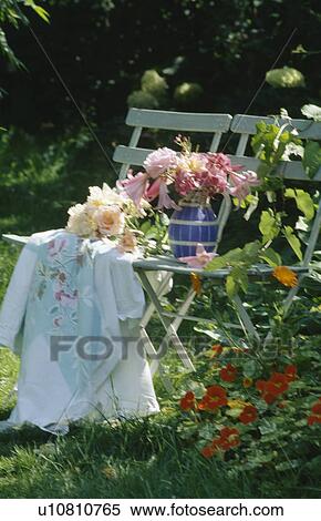 Stock Photography - Still-life of old tablecloth and jug of pink roses on garden chair. Fotosearch